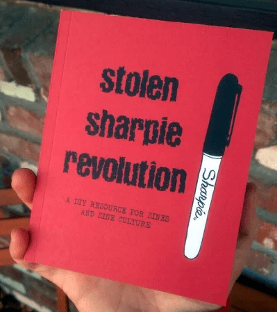 a hand holds a copy of the book "stolen sharpie revolution: a D.I.Y. resource for zines and zine culture"